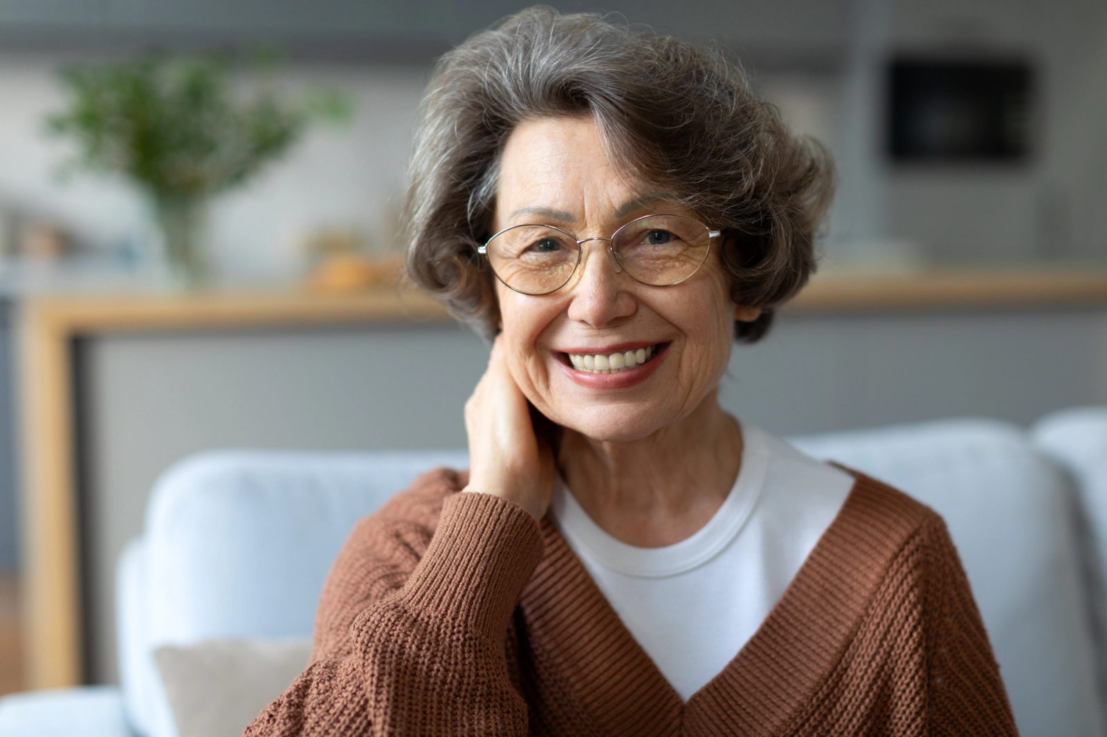 A smiling older woman with glasses and a brown sweater
