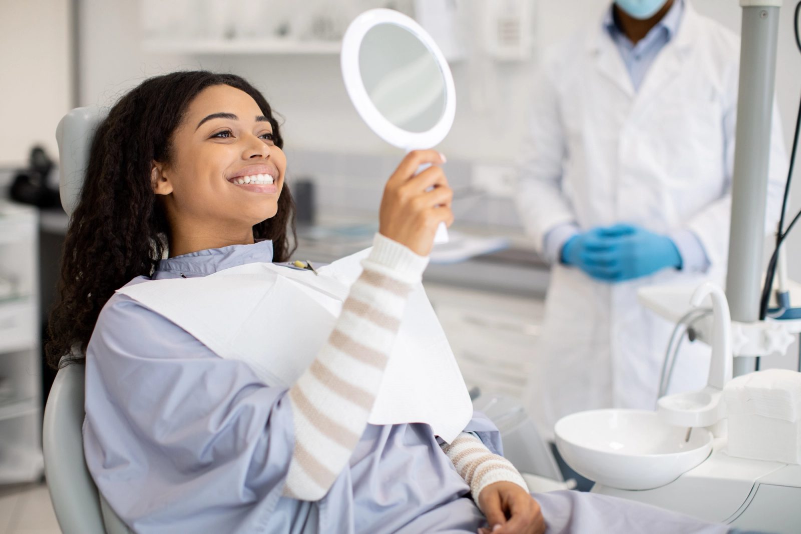 A smiling patient in a dental chair looks at her reflection