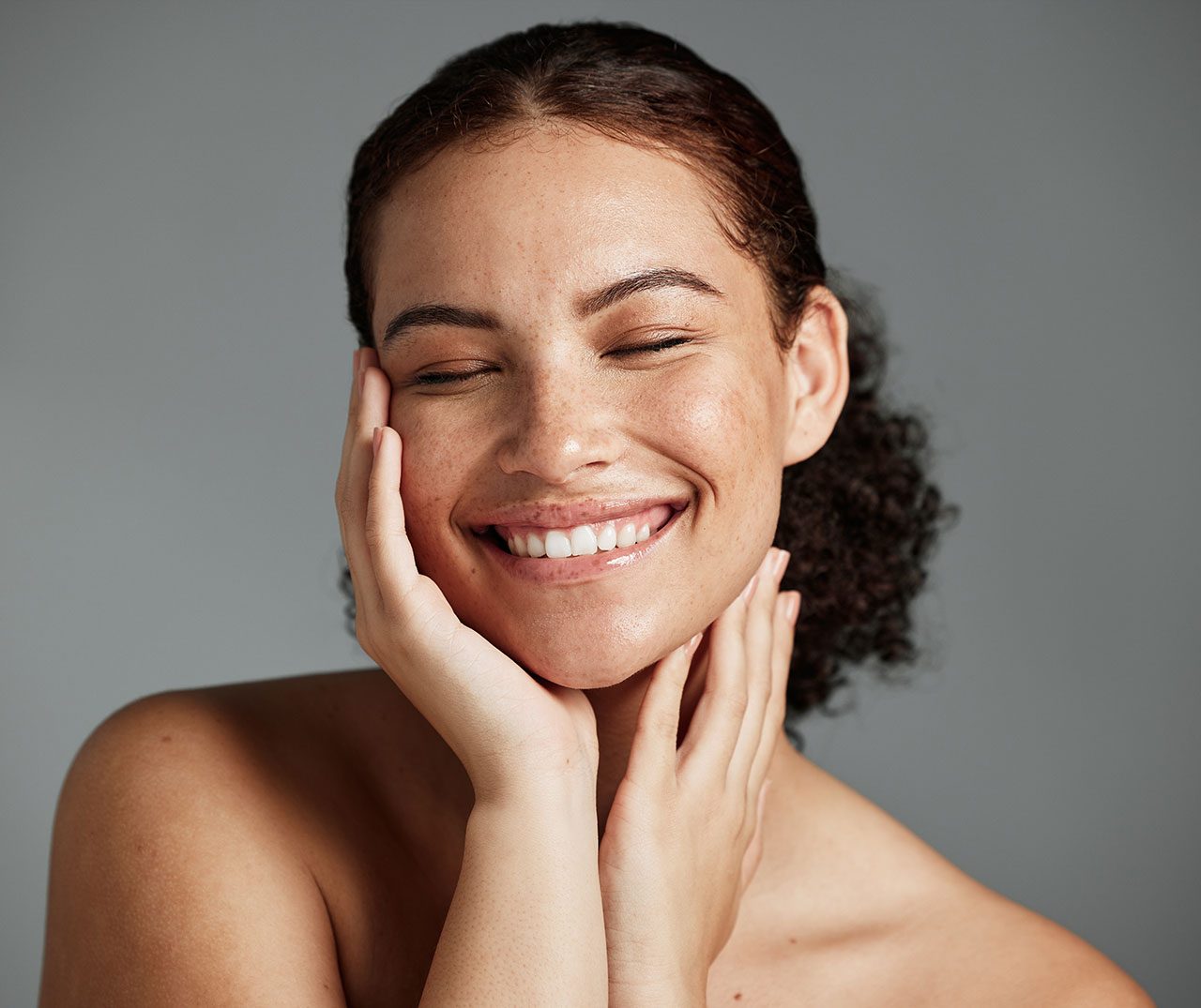 A smiling woman with freckles cups her face in her hands
