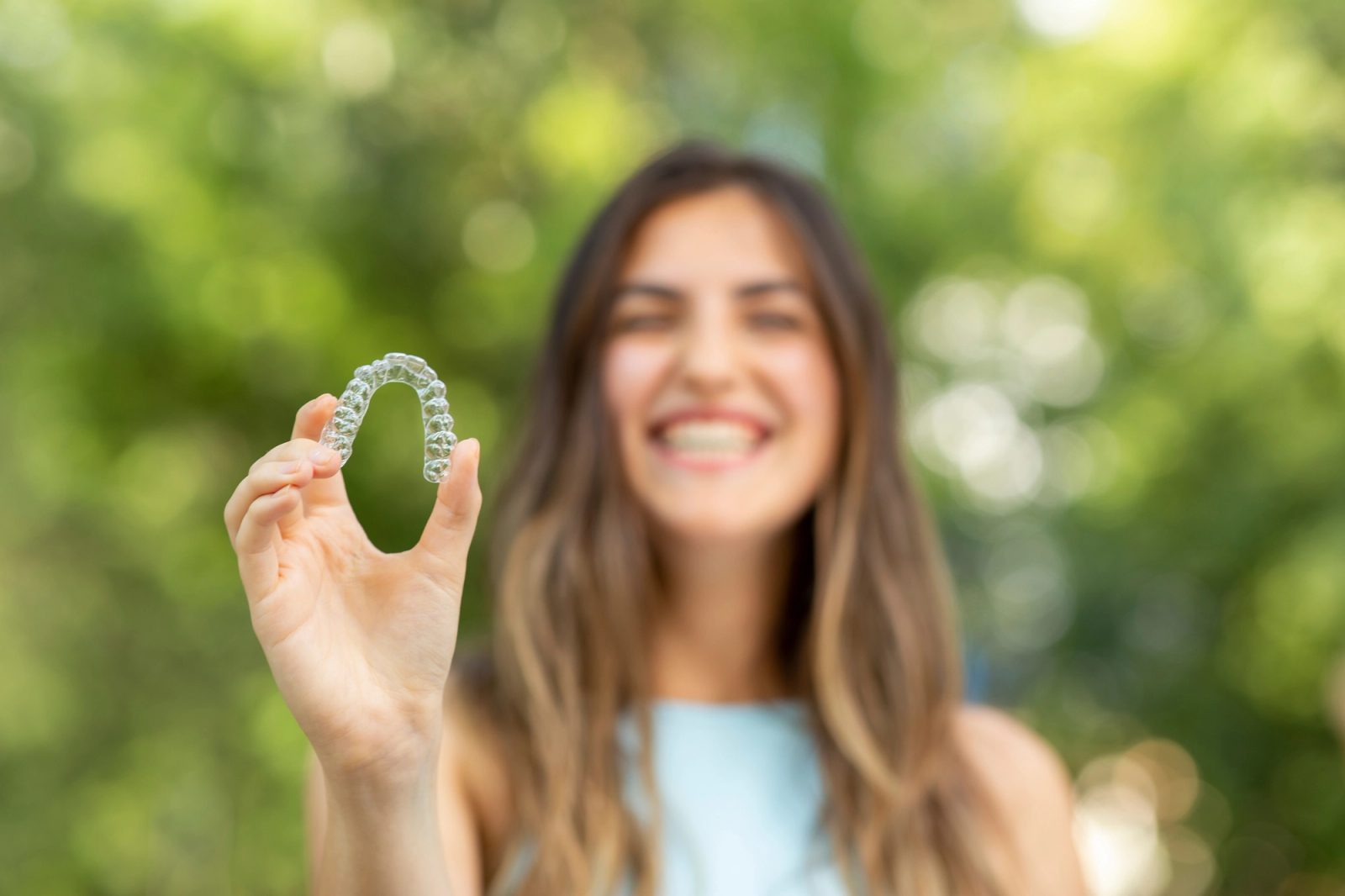 A smiling woman holds a clear dental aligner