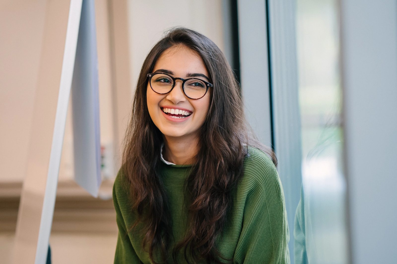 A young woman with long dark hair and glasses smiles widely