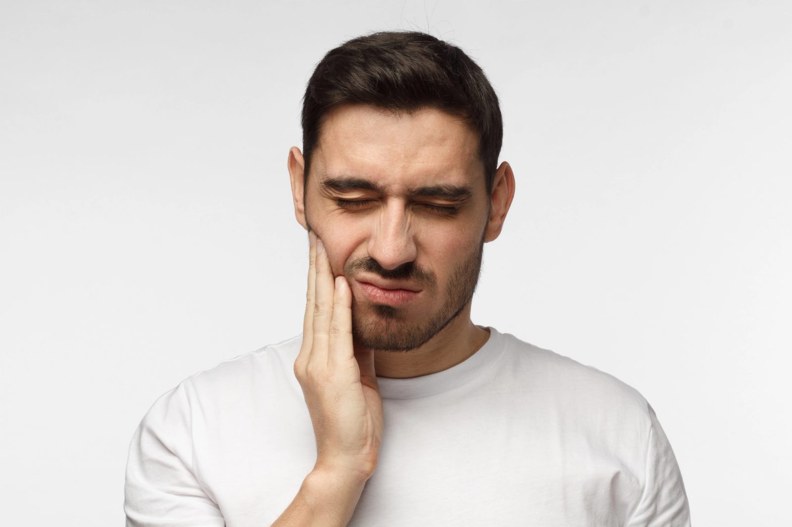 A man grimaces while holding his jaw