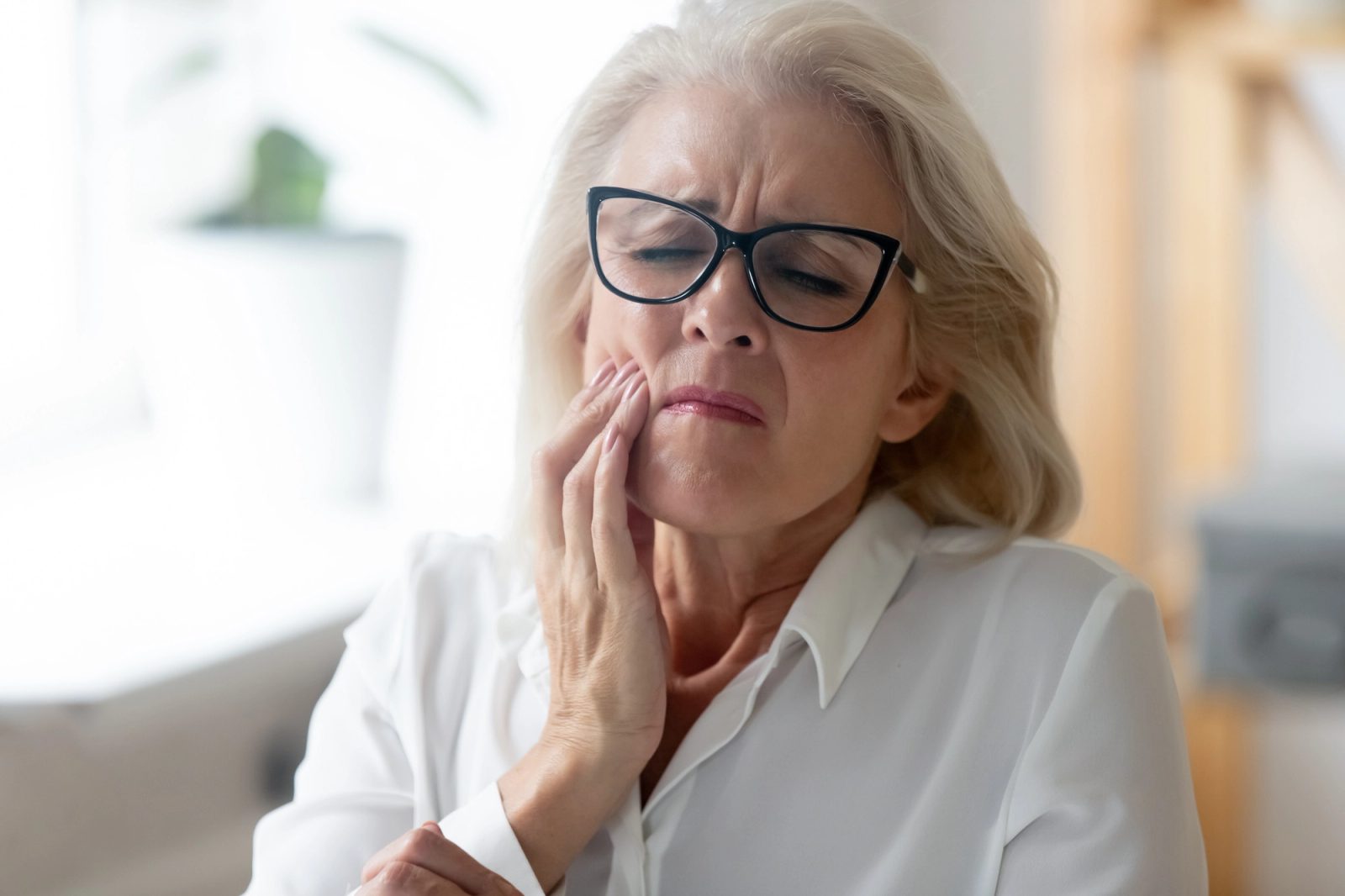 An older woman with glasses holds her mouth in pain