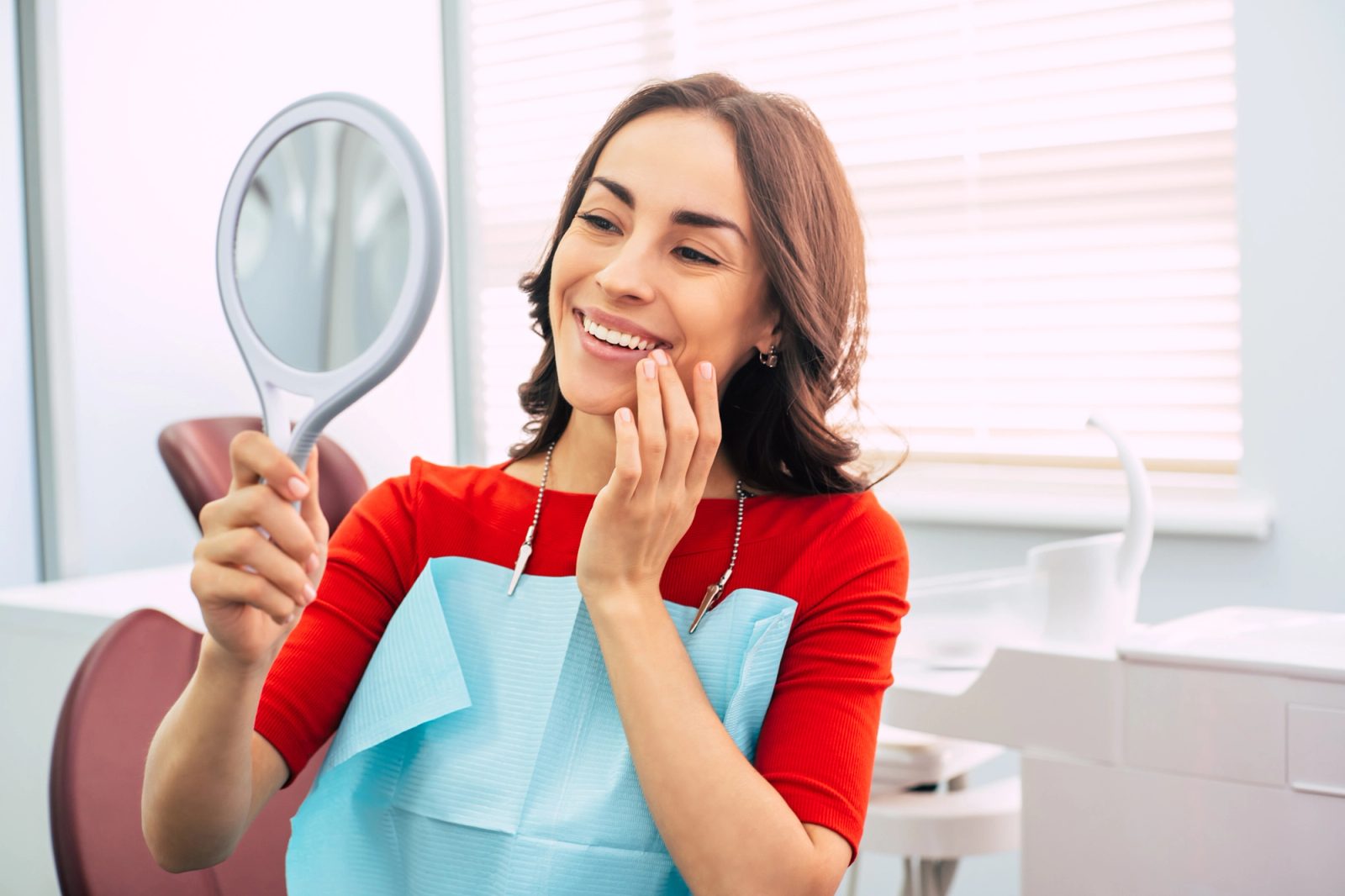 A dental patient smiles while looking into a handheld mirror