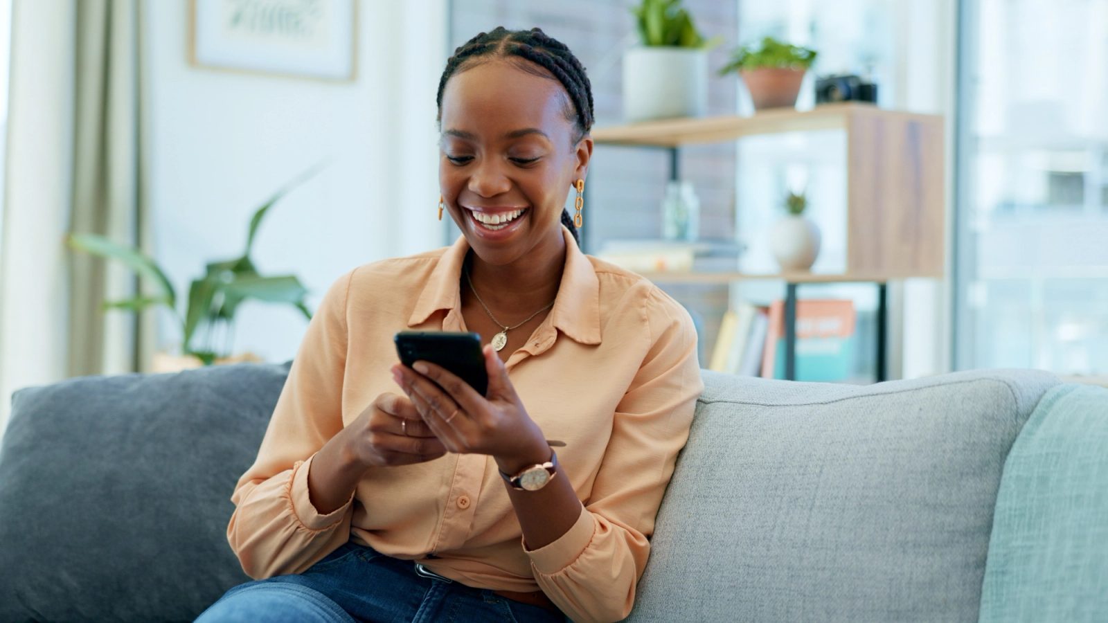A smiling woman sits on a couch and looks at her phone
