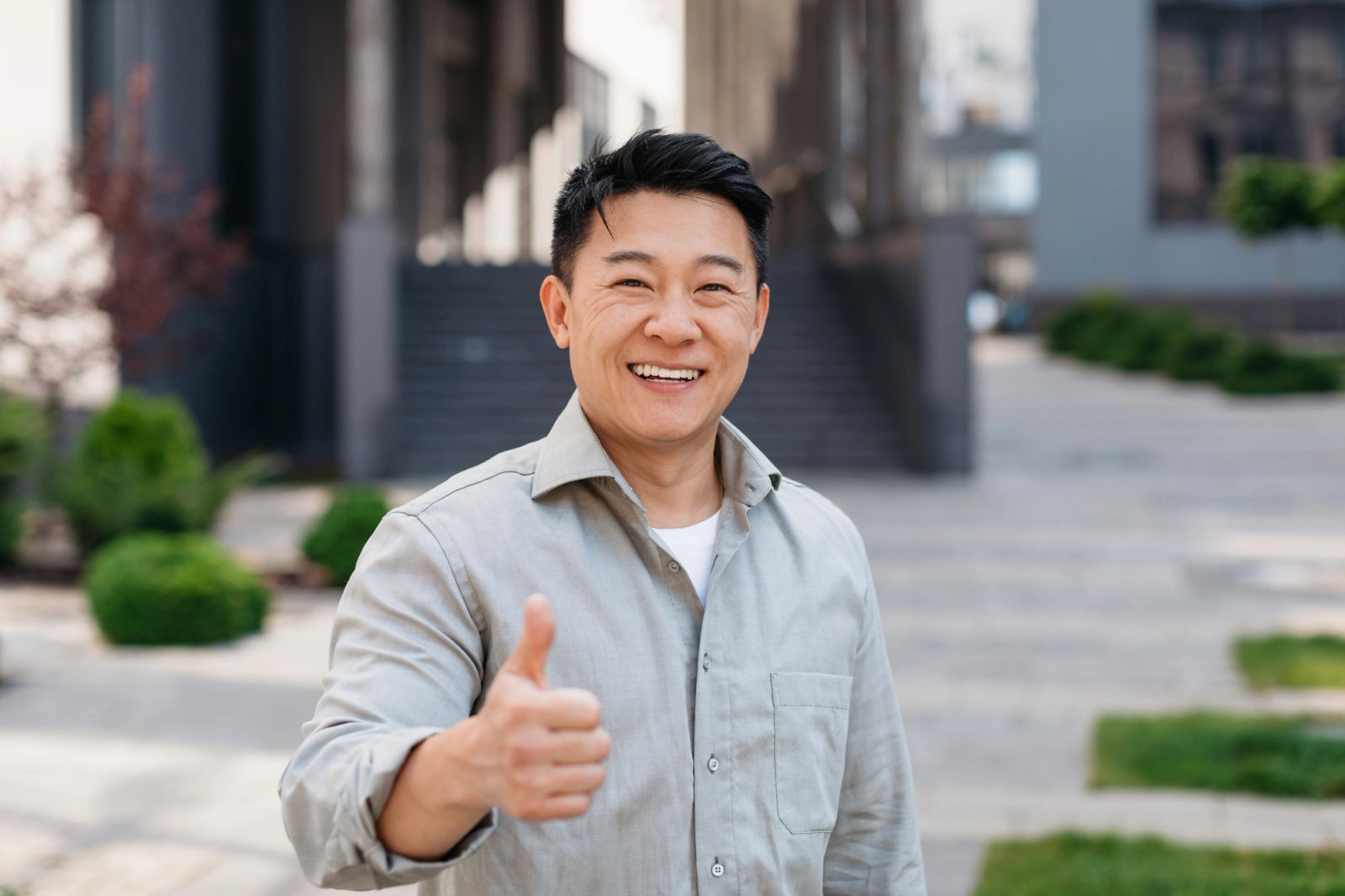 A smiling man gives a thumbs-up outdoors