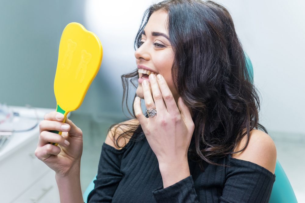 A woman checks her smile with a dental mirror