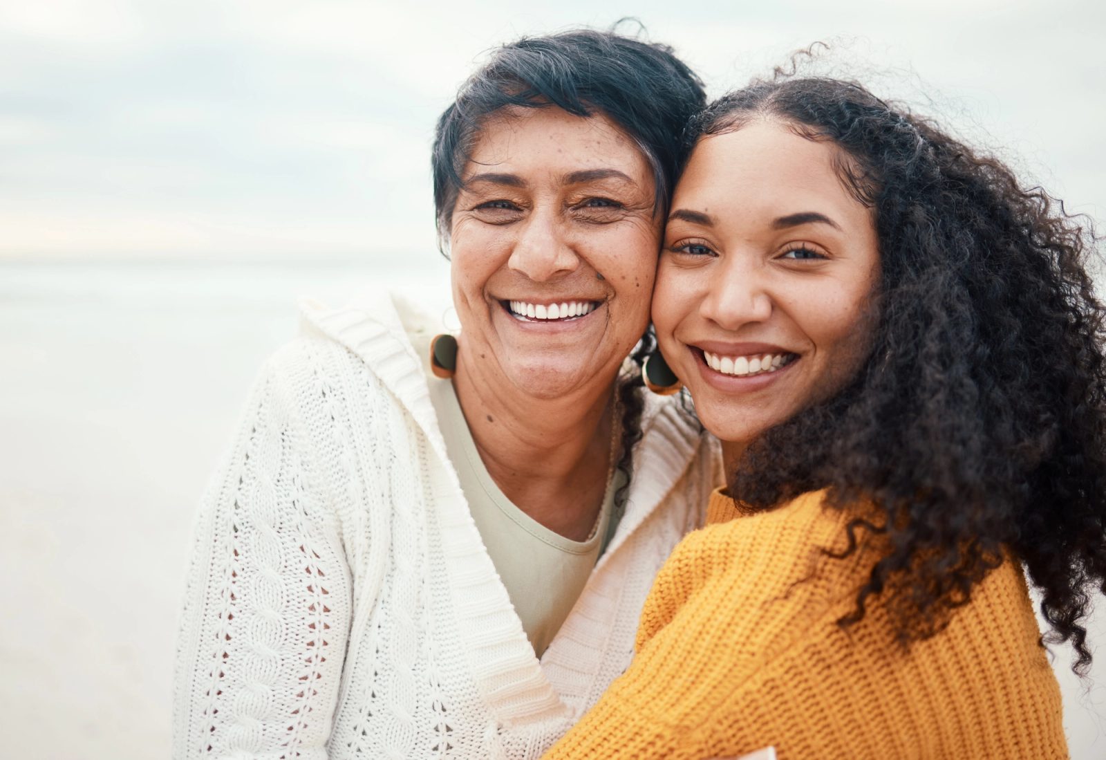 An older woman and a younger woman smile together on a beach