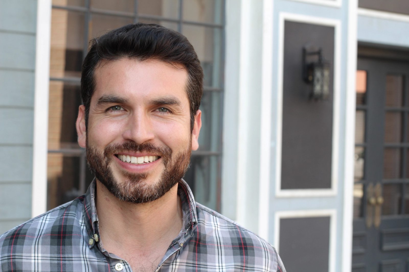 A smiling man with a beard wearing a plaid shirt