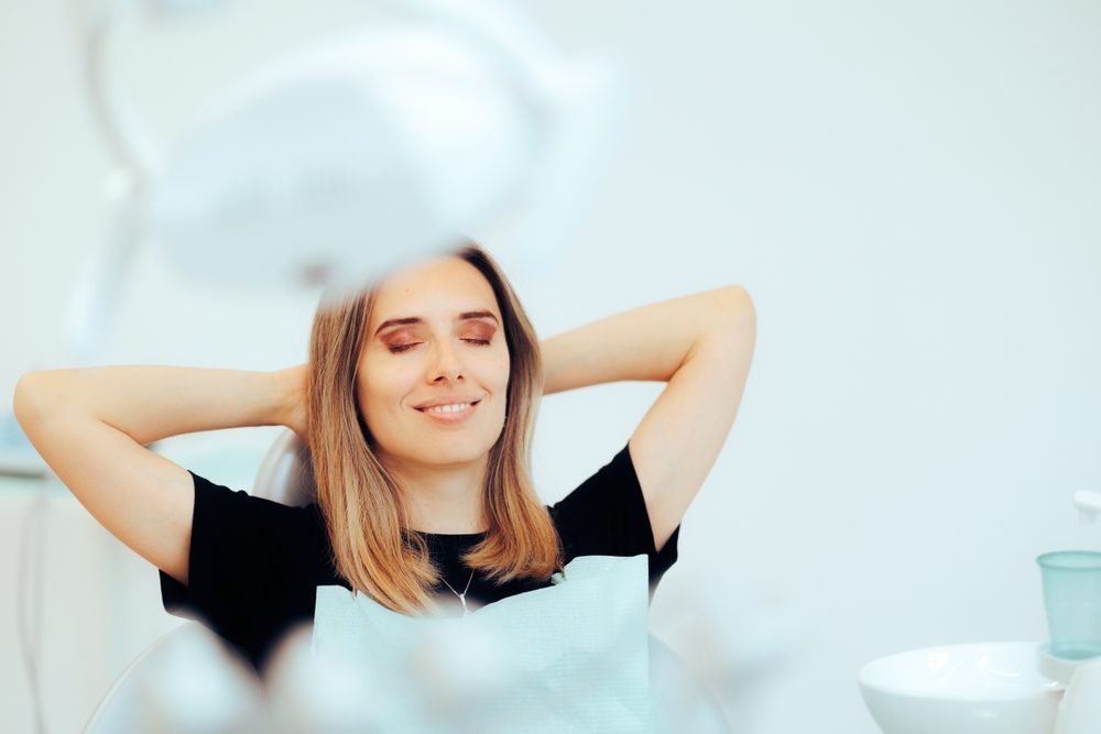 A relaxed patient rests in a dental chair with her eyes closed