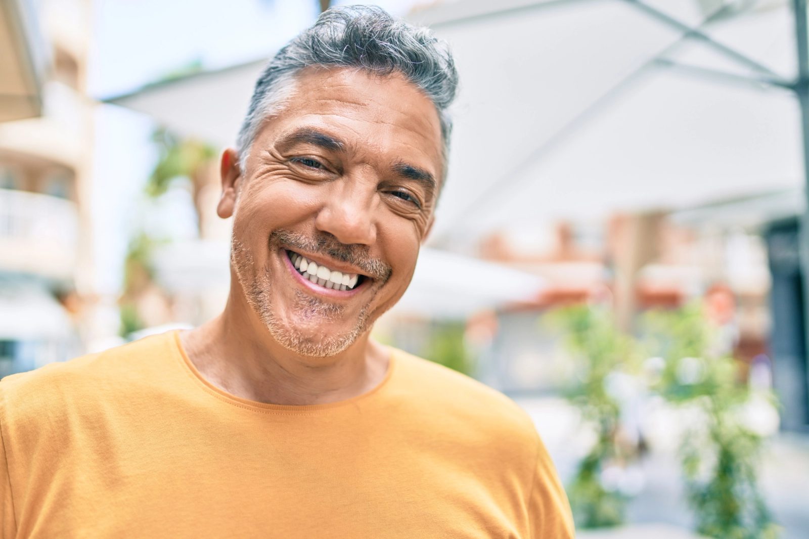 A smiling man with gray hair wearing a yellow shirt